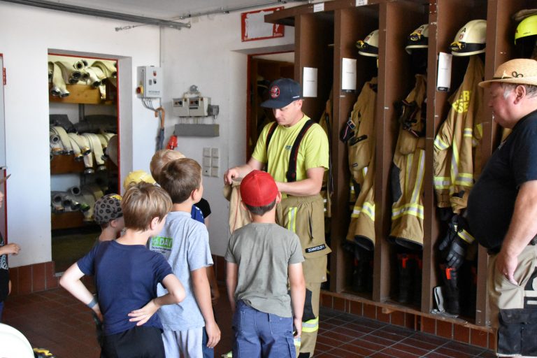Feuerwehrler zeigt Kindern die Feuerwehrkleidung